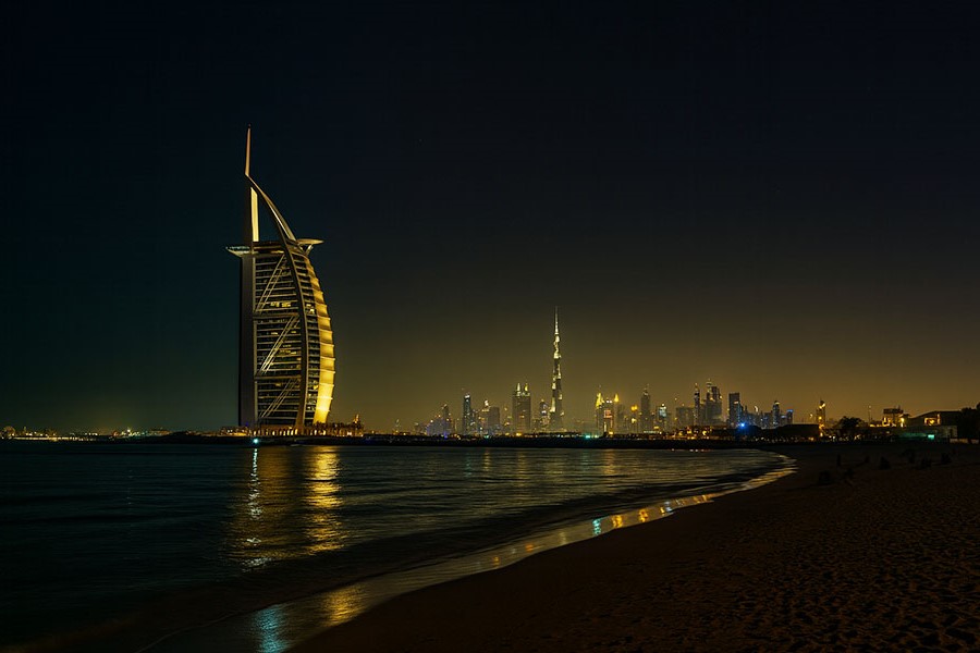 Calm and romantic beach setting at Dubai at night, with Burj al Arab and city's skyscrapers in the background.